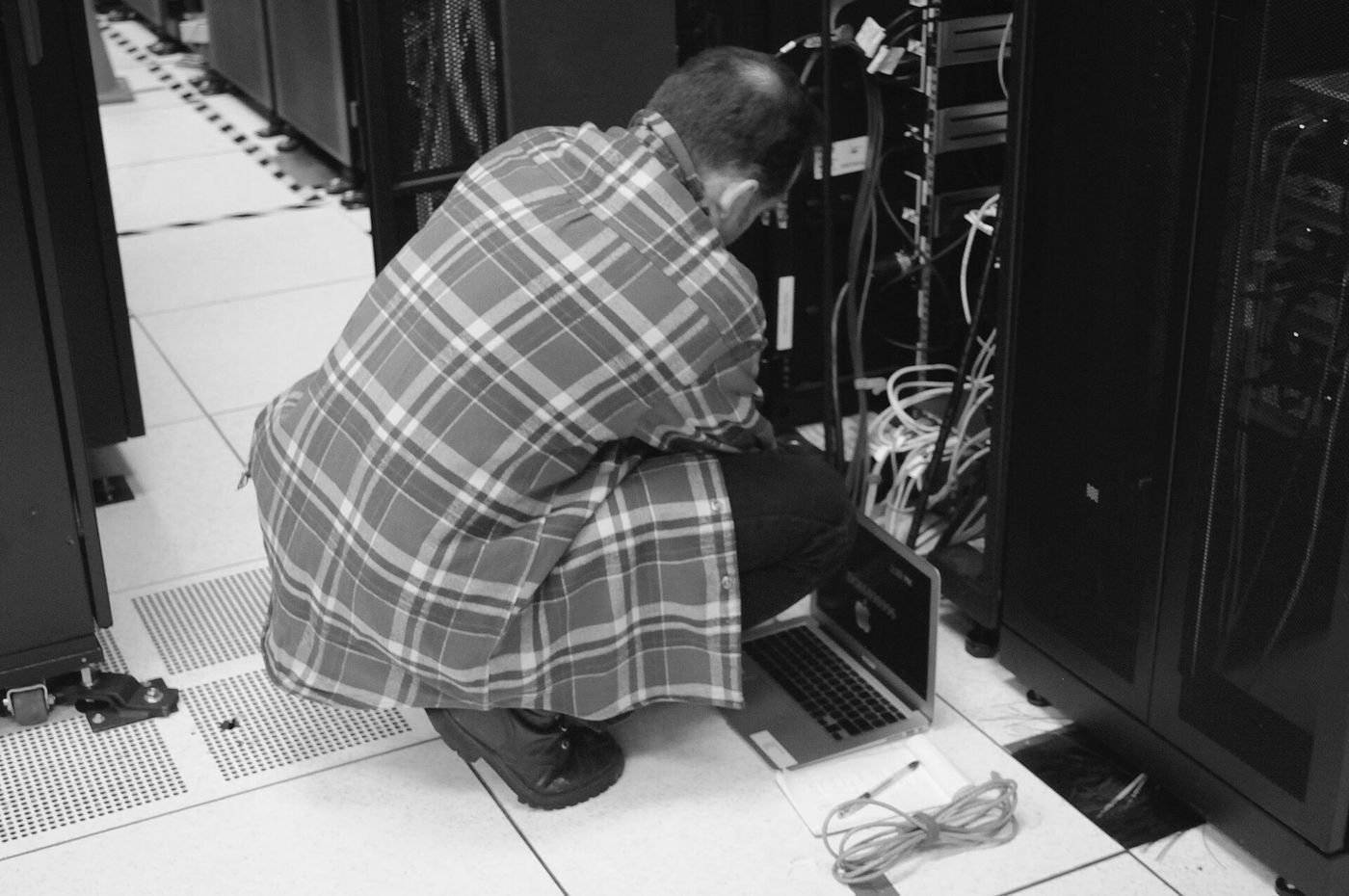 A technician with a laptop servicing a rack in a high-performance computing centre, checking cables and status lights
