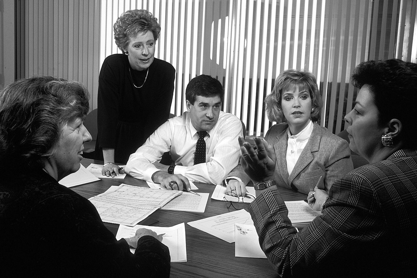 Five colleagues reviewing printed papers together around a conference room table