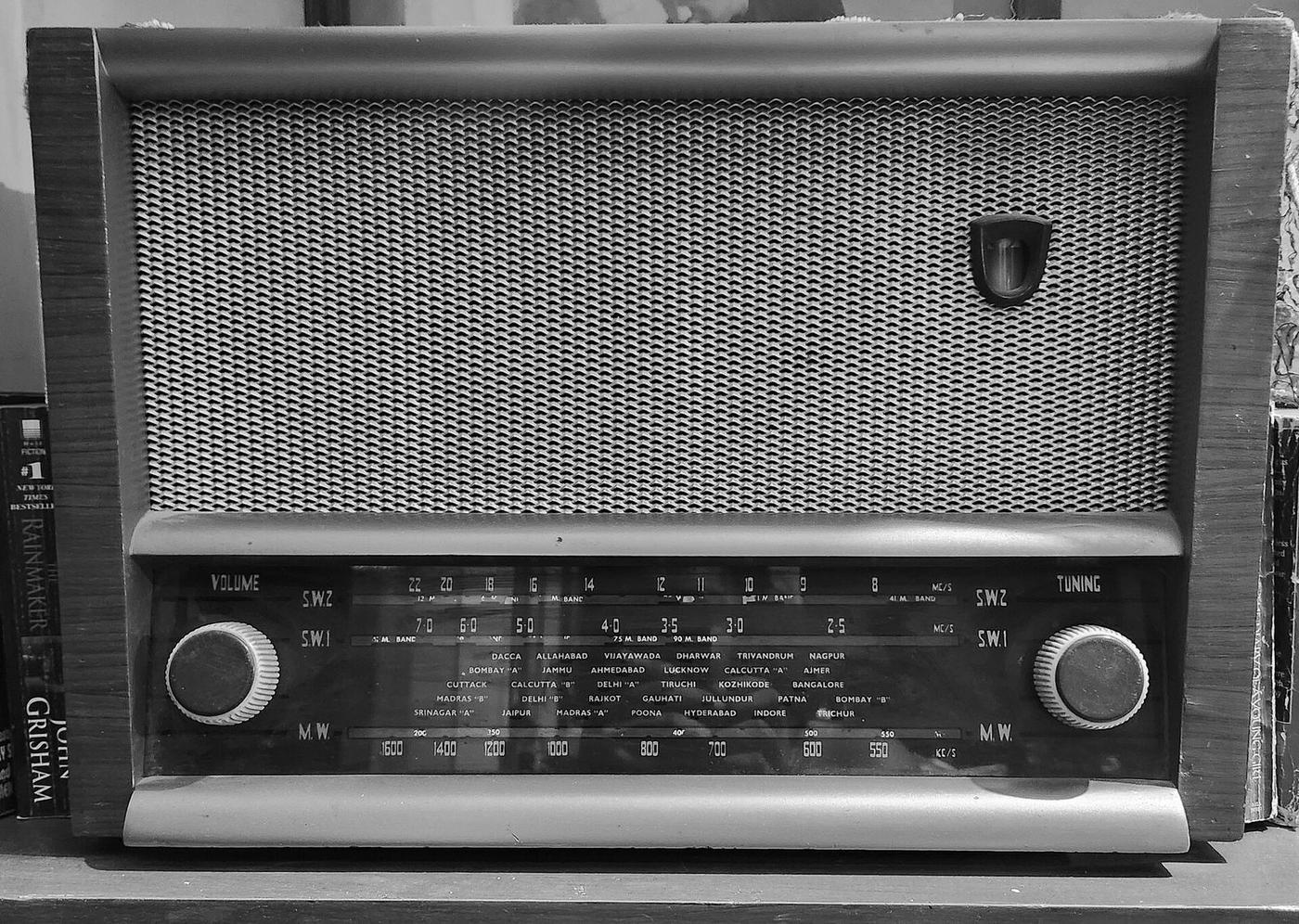 A wooden-cased vintage AM radio with a cream frequency dial and printed city presets
